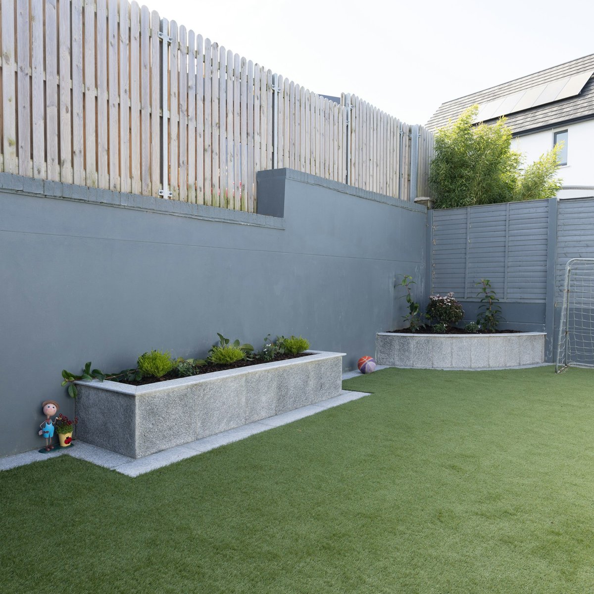 Finished artificial-turf backyard with raised stone planting beds and timber privacy fencing