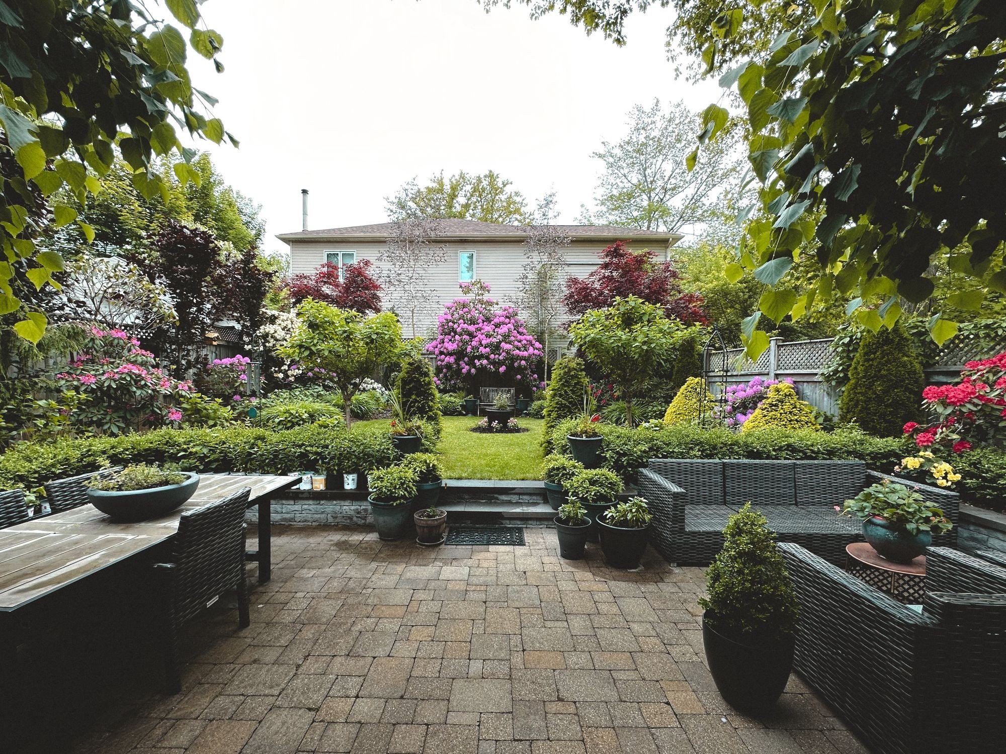 Finished backyard garden with a brick patio, green lawn, flowering shrubs and planted borders