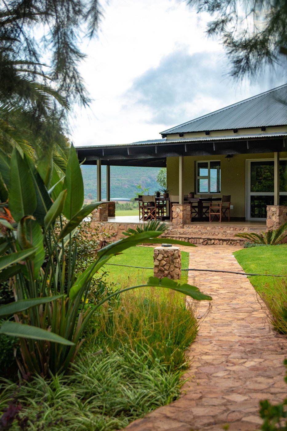 Finished stone garden walkway bordered by lawn and tropical planting leading to a covered patio